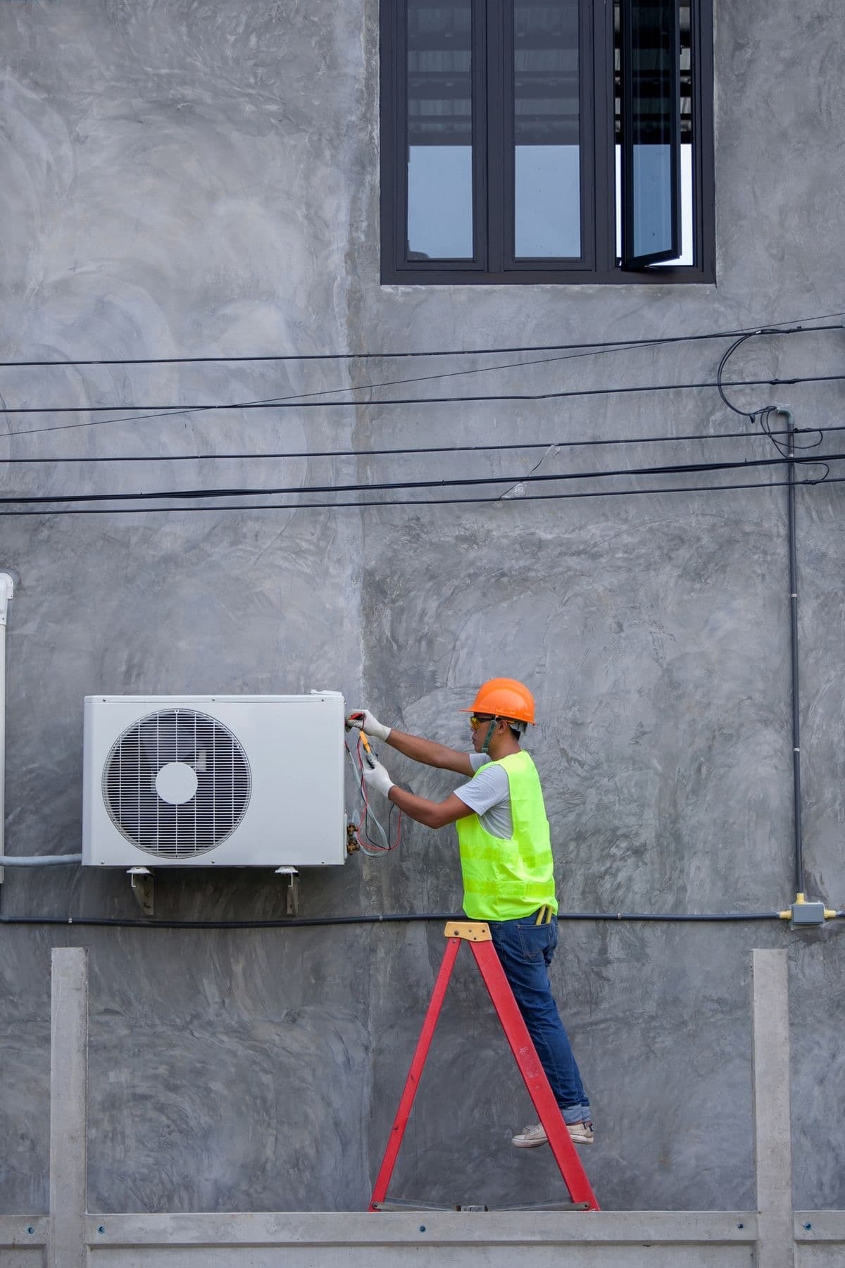 Technician on a ladder using a multimeter to service an outdoor AC condenser unit