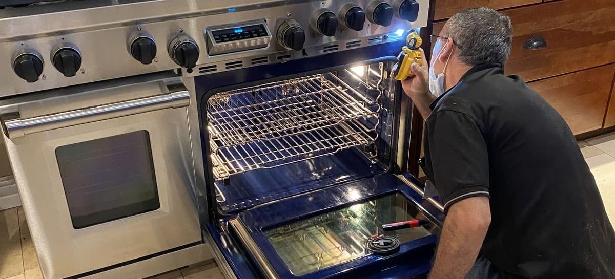 Technician using a diagnostic tool to inspect an open range oven