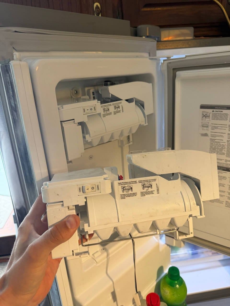 An ice maker assembly removed from a refrigerator freezer door, held in hand