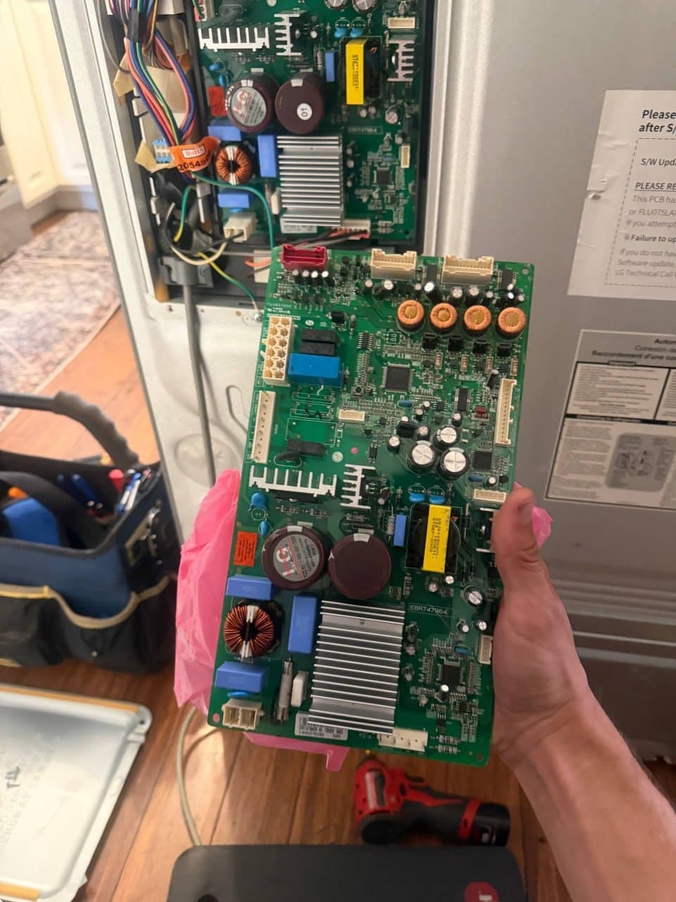 A replacement refrigerator control board held in hand before installation